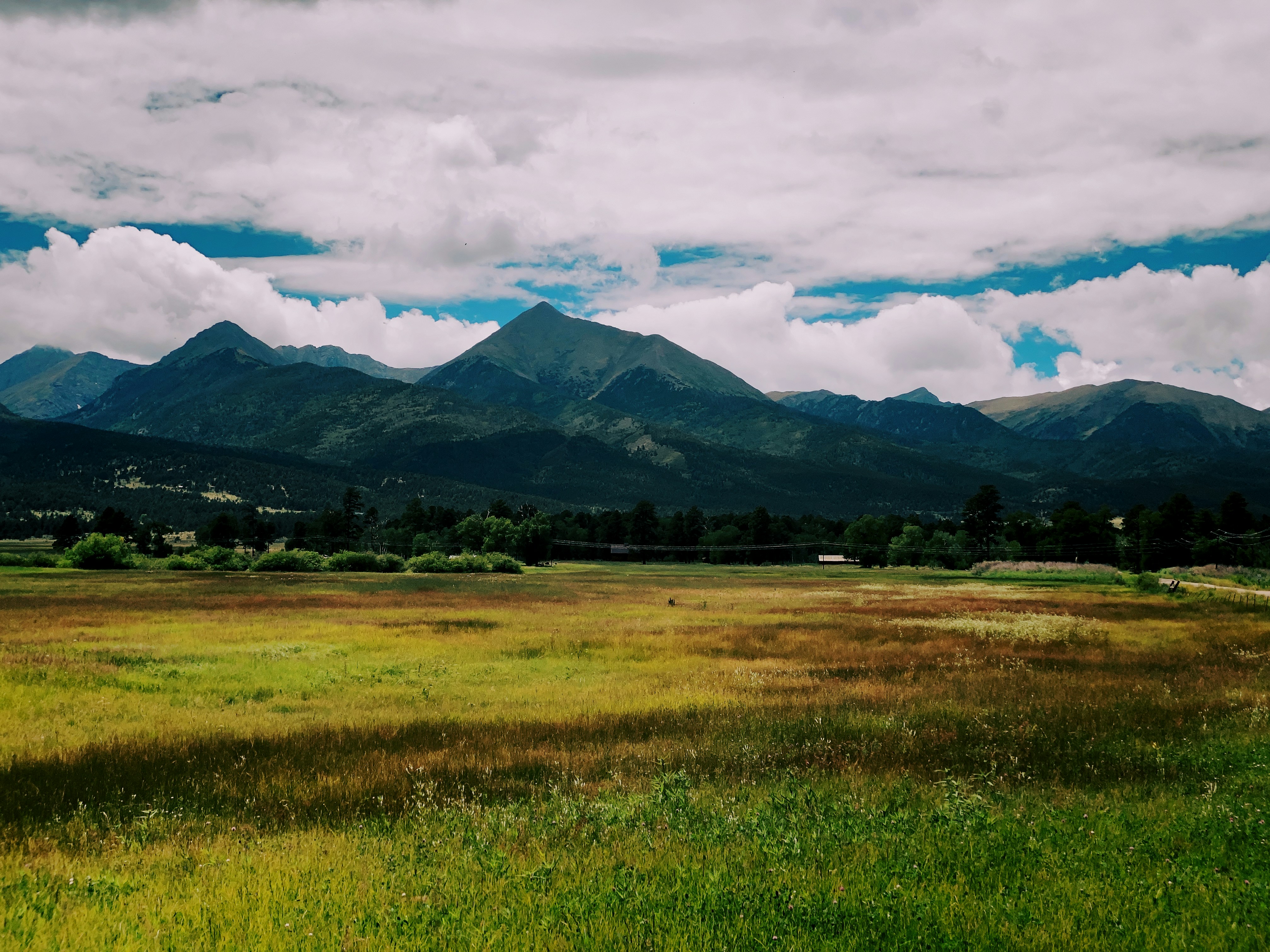 green grass field near mountain under cloudy sky during daytime