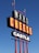 A tall outdoor sign with large bold letters reads 'MARS CHEESE CASTLE'. It is supported by red poles and is set against a clear blue sky. Two flags, including an American flag, are flying at the top.