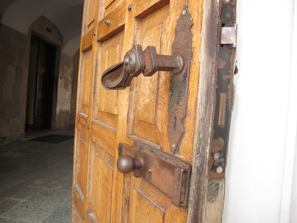 A sturdy, large wooden door with intricate carvings, slightly ajar to reveal warm light inside.