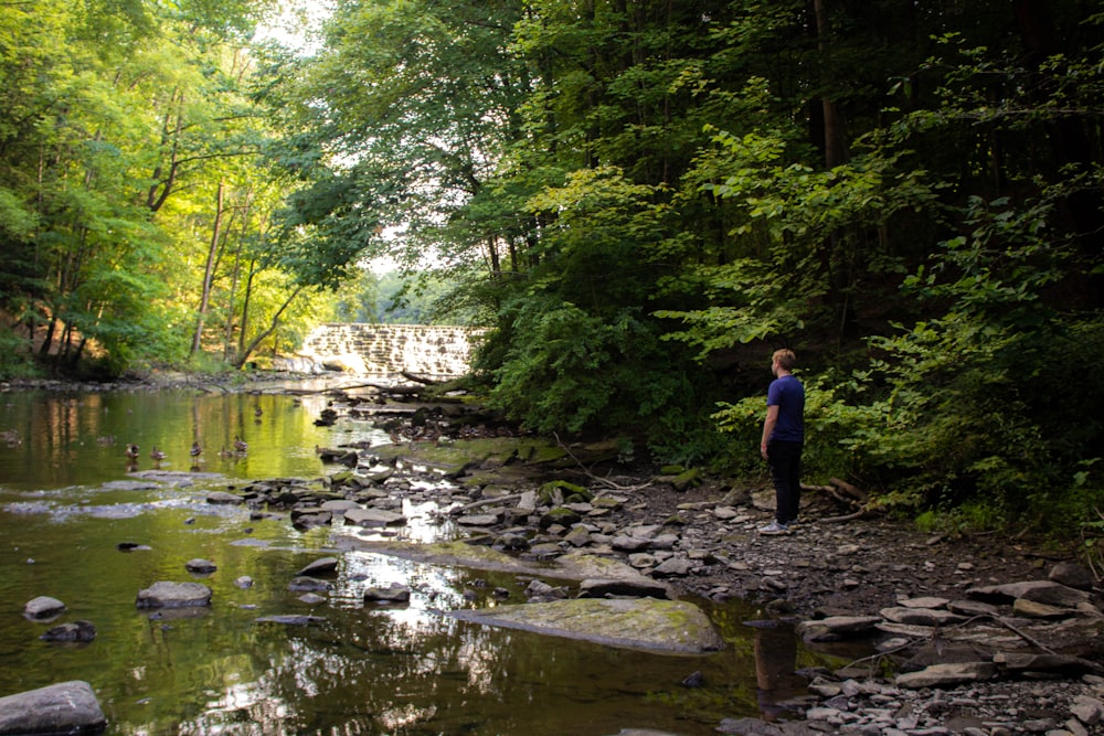 man in blue jacket standing on rock near river during daytime