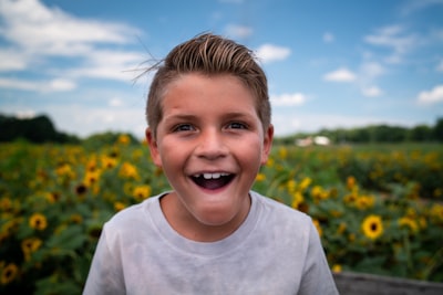 boy in white crew neck shirt standing on yellow flower field during daytime excited google meet background