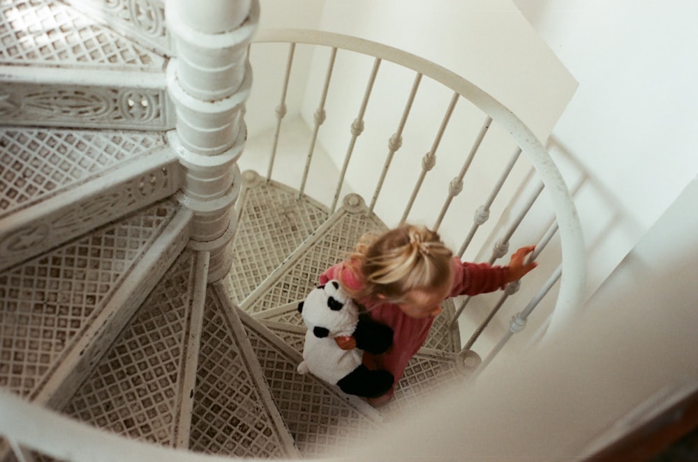girl in red long sleeve shirt and black pants climbing on white wooden spiral staircase