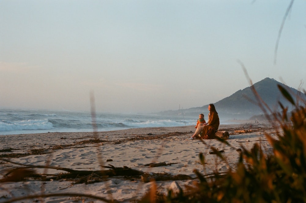 woman in brown dress lying on brown sand near body of water during daytime