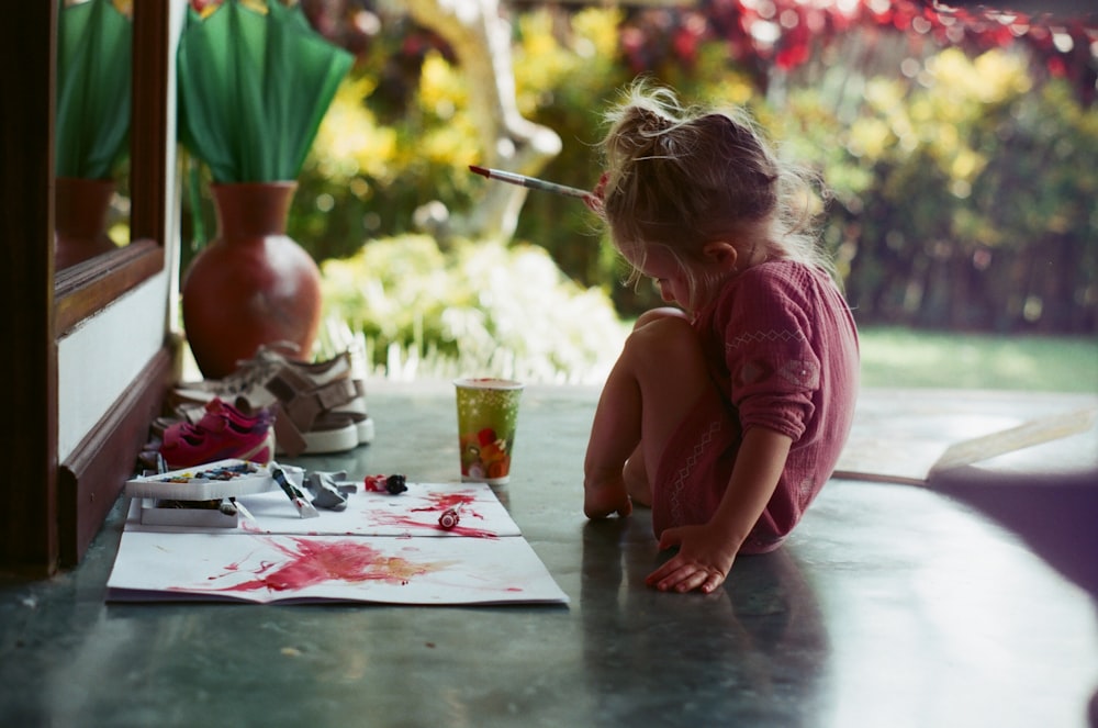 girl in pink shirt sitting on floor while writing