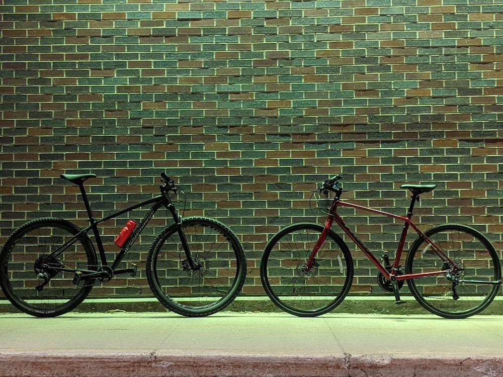 red and black mountain bike leaning on brown brick wall