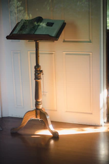 An open Bible resting on a wooden lectern bathed in warm sunlight streaming through stained glass.