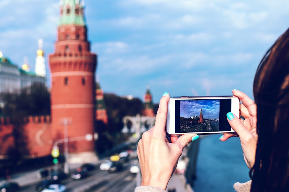 Person mit weißem Android-Smartphone beim Fotografieren des Turms tagsüber