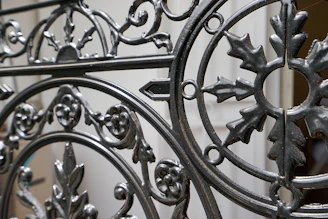 Ornate wrought iron gate featuring intricate patterns and designs with a mix of curved and linear elements. The craftsmanship includes floral and leaf motifs, highlighting a vintage or historical style.