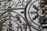 Ornate wrought iron gate featuring intricate patterns and designs with a mix of curved and linear elements. The craftsmanship includes floral and leaf motifs, highlighting a vintage or historical style.