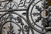 Ornate wrought iron gate featuring intricate patterns and designs with a mix of curved and linear elements. The craftsmanship includes floral and leaf motifs, highlighting a vintage or historical style.