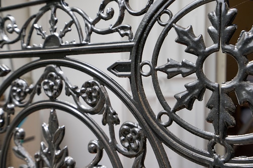 Ornate wrought iron gate featuring intricate patterns and designs with a mix of curved and linear elements. The craftsmanship includes floral and leaf motifs, highlighting a vintage or historical style.