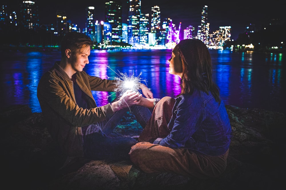 man and woman sitting on rock with fireworks display