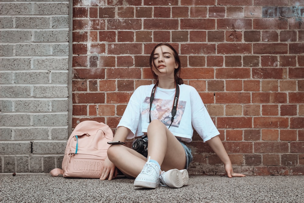 woman in white shirt and blue denim shorts sitting on brown concrete brick wall