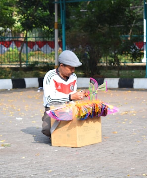 man in white and black shirt and white cap sitting on brown cardboard box