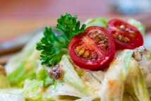 A close-up of a fresh salad featuring sliced red cherry tomatoes and creamy dressing. The salad also includes leafy greens and a sprig of parsley for garnish.