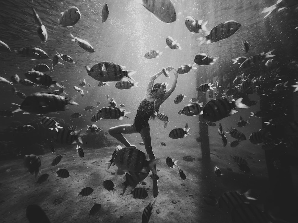 grayscale photo of man in black jacket and pants standing in front of fish