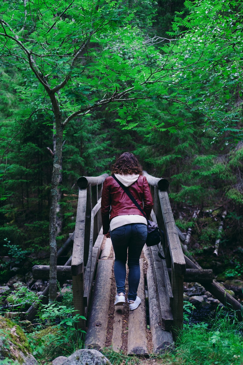 a woman walking across a wooden bridge in the woods