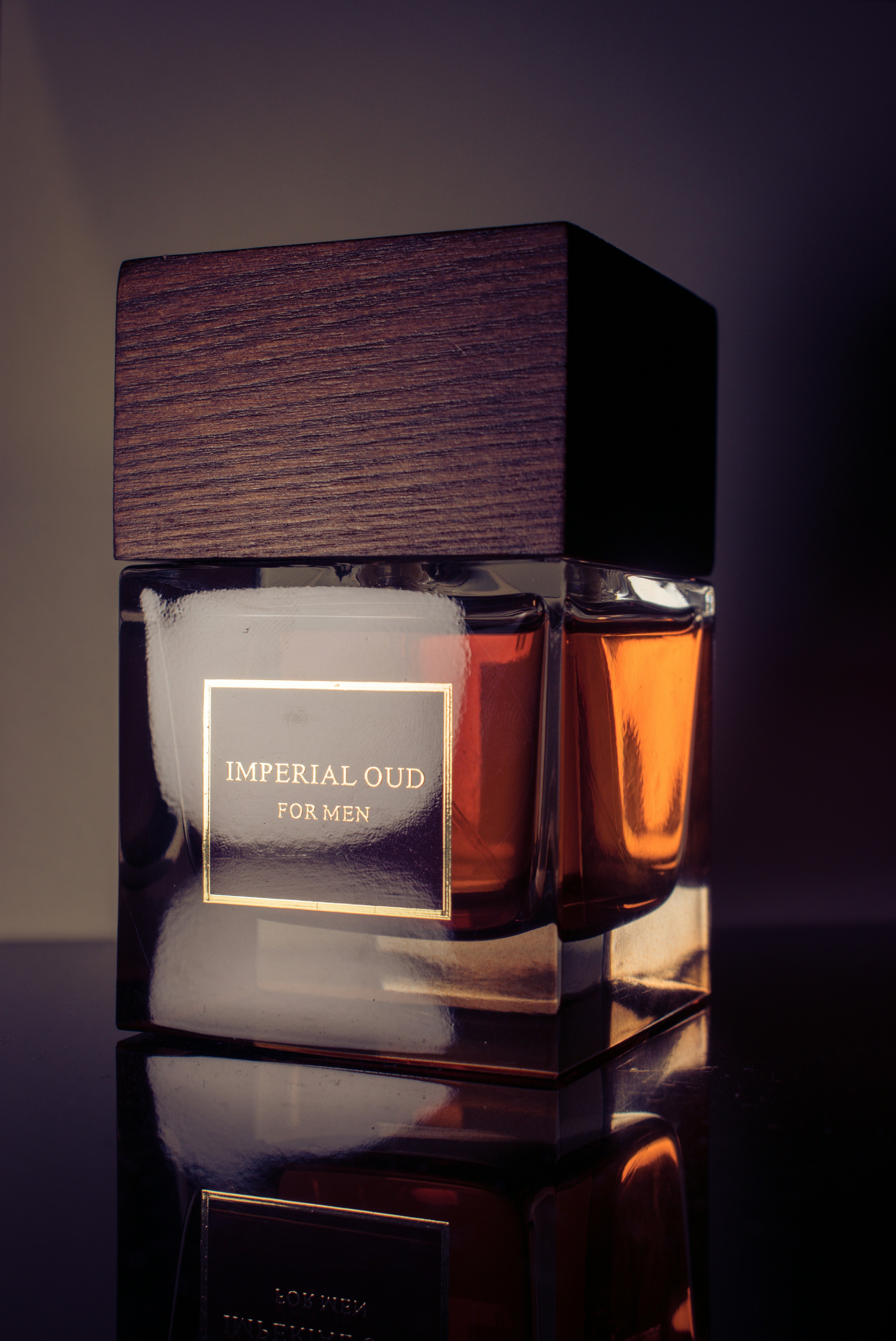 A sleek perfume bottle with a wooden cap is prominently displayed. The label reads 'Imperial Oud for Men'. The design combines glass and wood, giving it an elegant and masculine appearance. The lighting highlights the rich amber liquid inside.