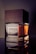 A sleek perfume bottle with a wooden cap is prominently displayed. The label reads 'Imperial Oud for Men'. The design combines glass and wood, giving it an elegant and masculine appearance. The lighting highlights the rich amber liquid inside.