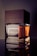 A sleek perfume bottle with a wooden cap is prominently displayed. The label reads 'Imperial Oud for Men'. The design combines glass and wood, giving it an elegant and masculine appearance. The lighting highlights the rich amber liquid inside.