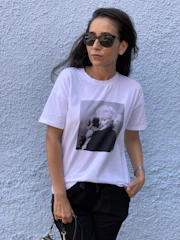 A model wearing a vintage-style t-shirt with a faded logo, standing against a brick wall.