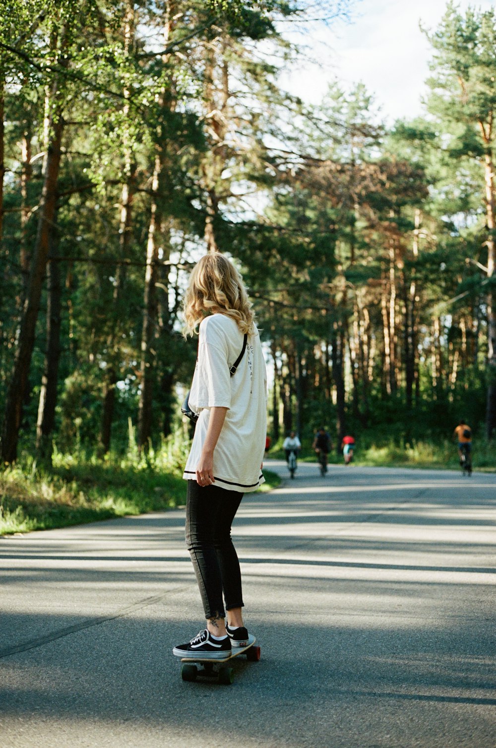 mulher na camisa branca de manga comprida e calças pretas andando na estrada durante o dia
