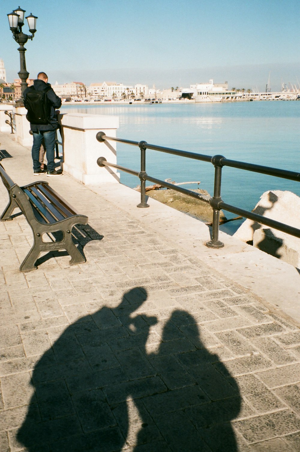 man in black jacket standing on gray concrete floor near body of water during daytime