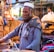 A smiling middle-aged man standing in front of a colorful Bikaner street market.