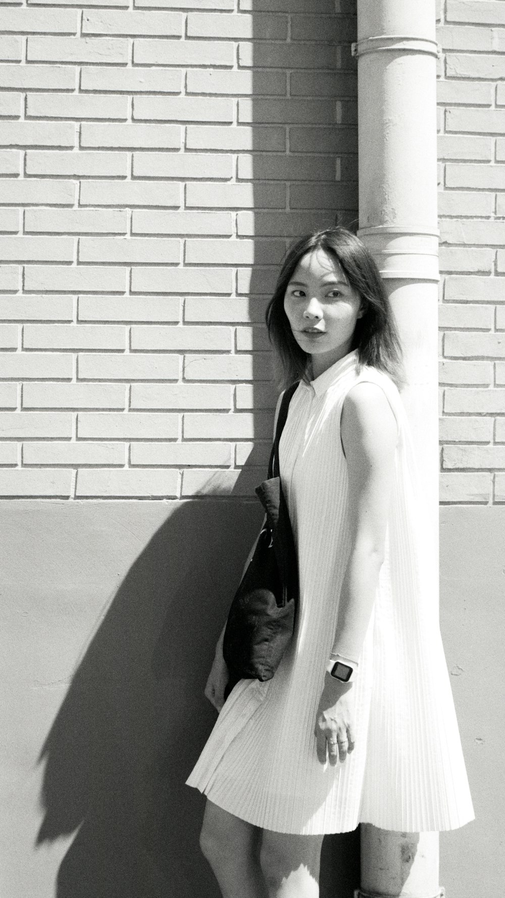 woman in white sleeveless dress standing beside brick wall