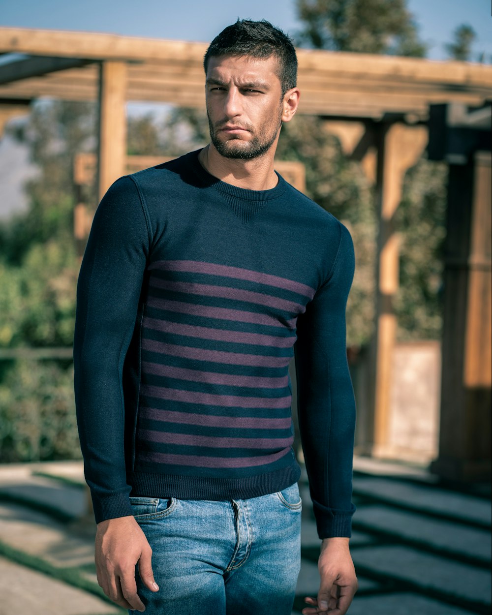 man in blue long sleeve shirt and blue denim jeans standing on brown wooden bridge during