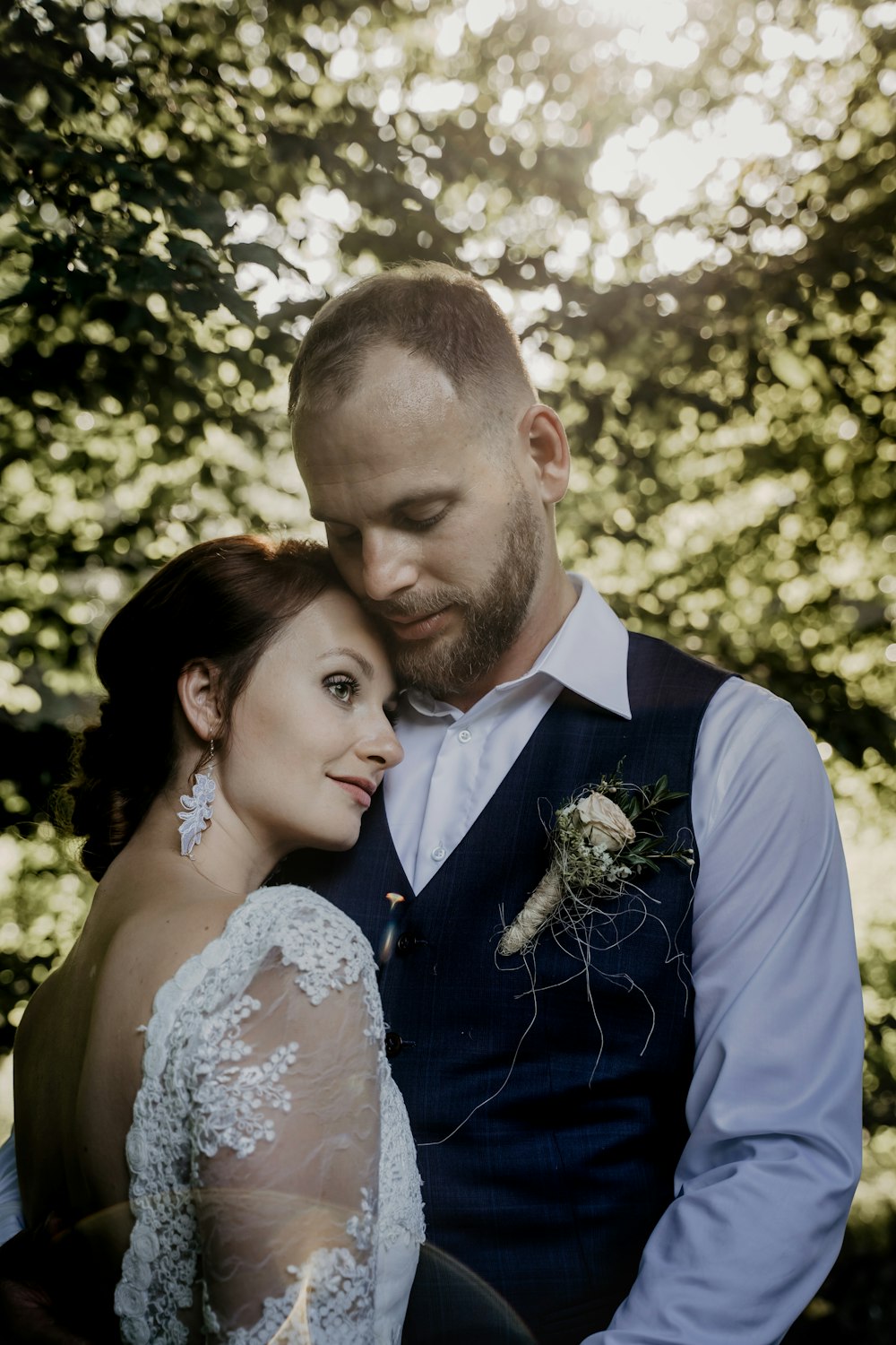 man in blue suit jacket kissing woman in white floral lace wedding dress