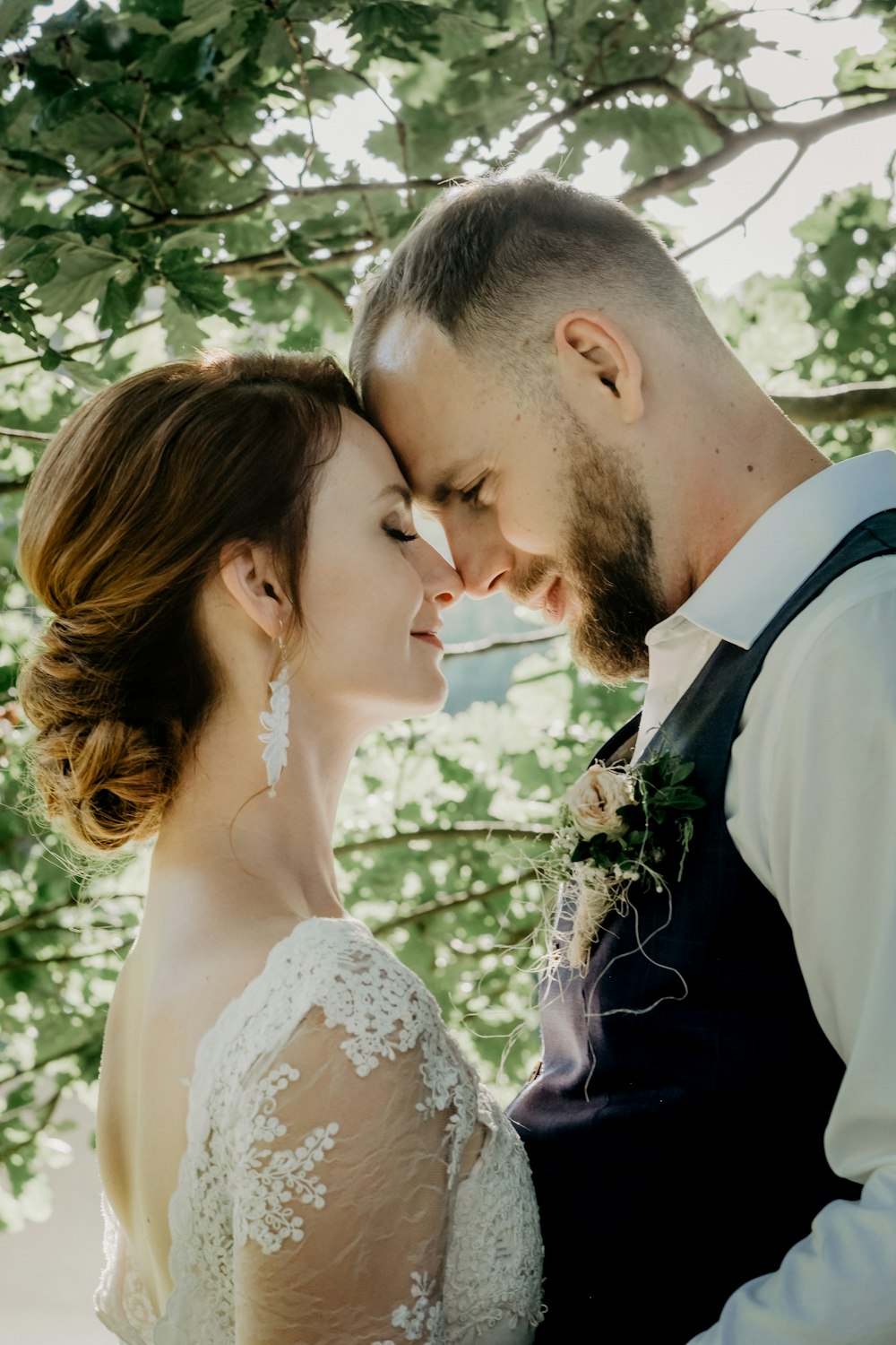 man in black suit kissing woman in white floral lace wedding dress