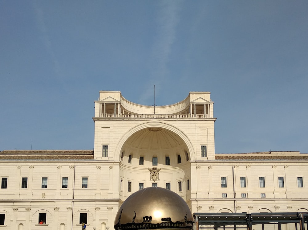a large white building with a large metal ball in front of it