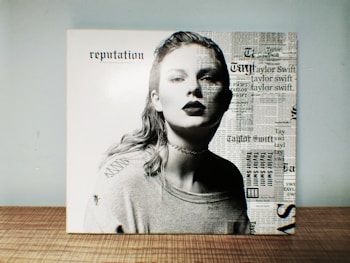 A black and white portrait of a person with a serious expression, wearing a choker and a sweater. The right half of the image is overlaid with newspaper-style text, featuring repeated mentions of a name. The background is plain.