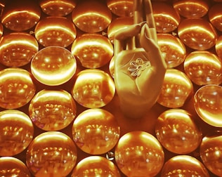 A golden hand positioned in a gesture commonly associated with meditation, surrounded by numerous shiny circular discs that create a textured backdrop. The discs reflect light, contributing to a luminous and harmonious visual effect.