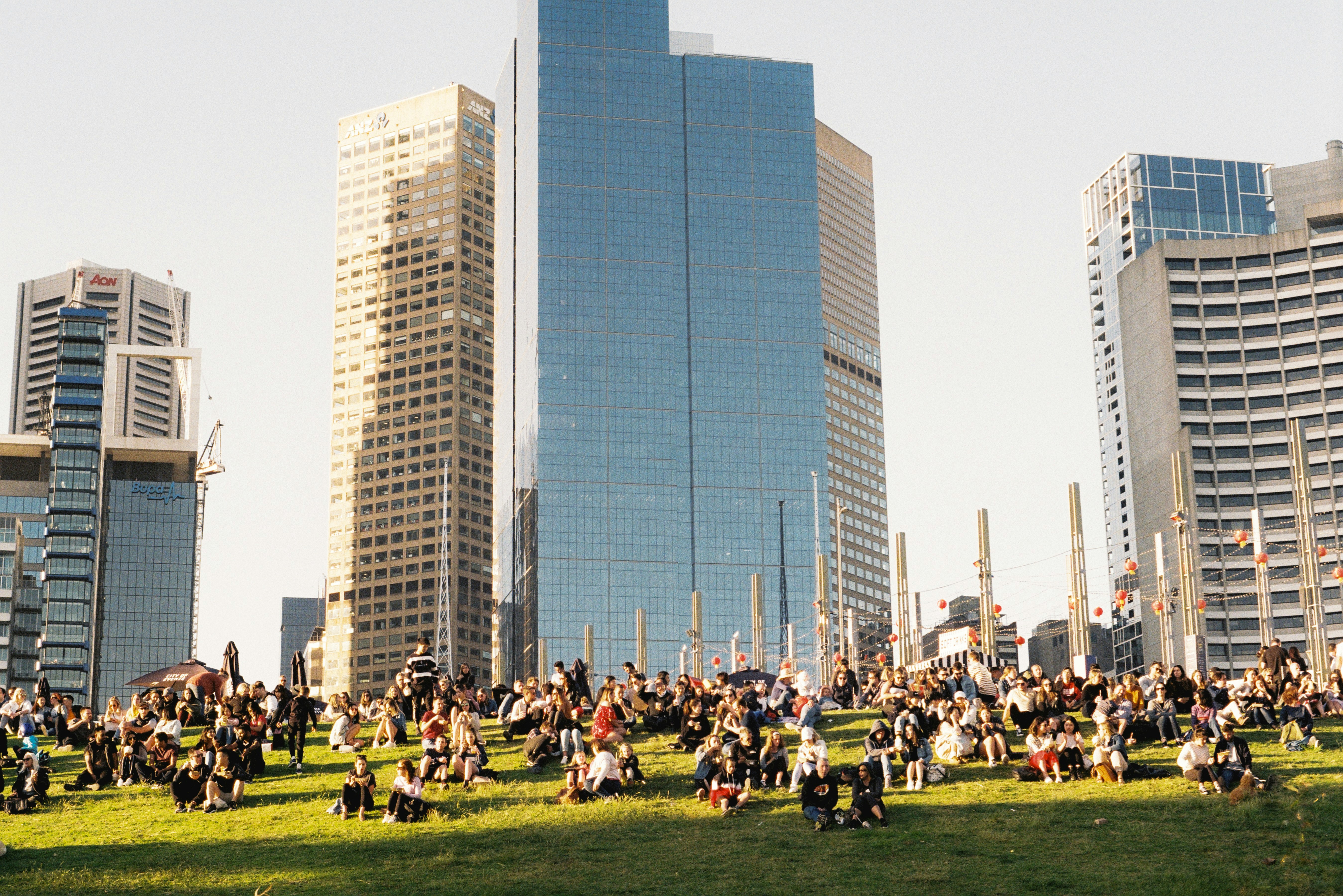 people sitting on green grass field near high rise building during daytime