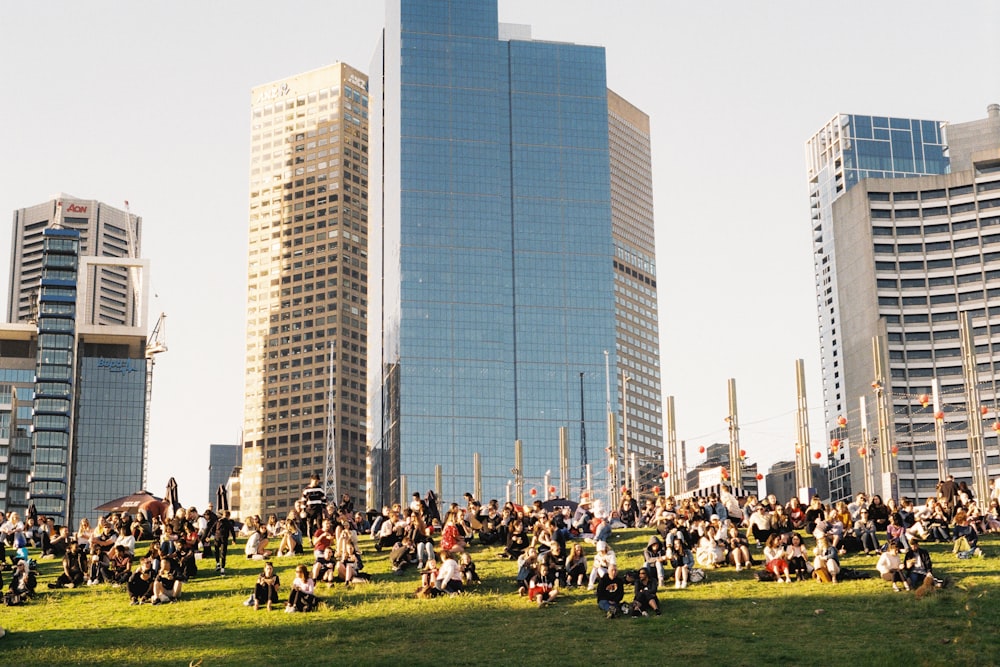 people sitting on green grass field near high rise building during daytime