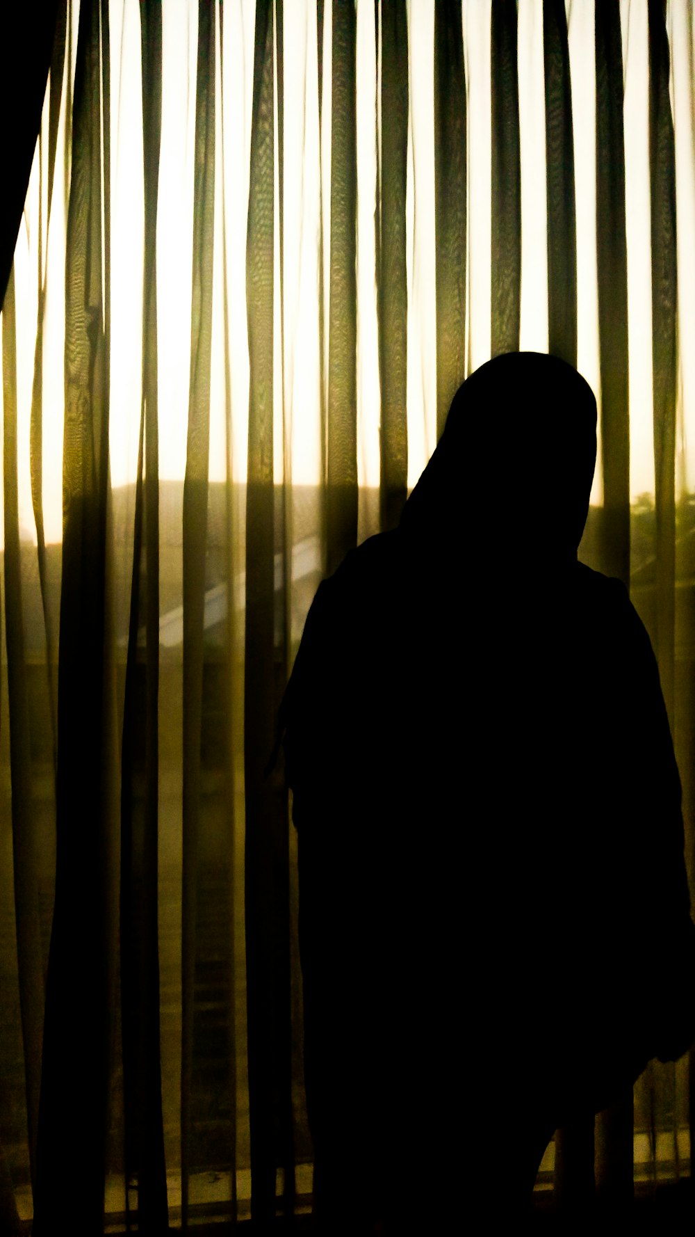 silhouette of person standing near white window curtain