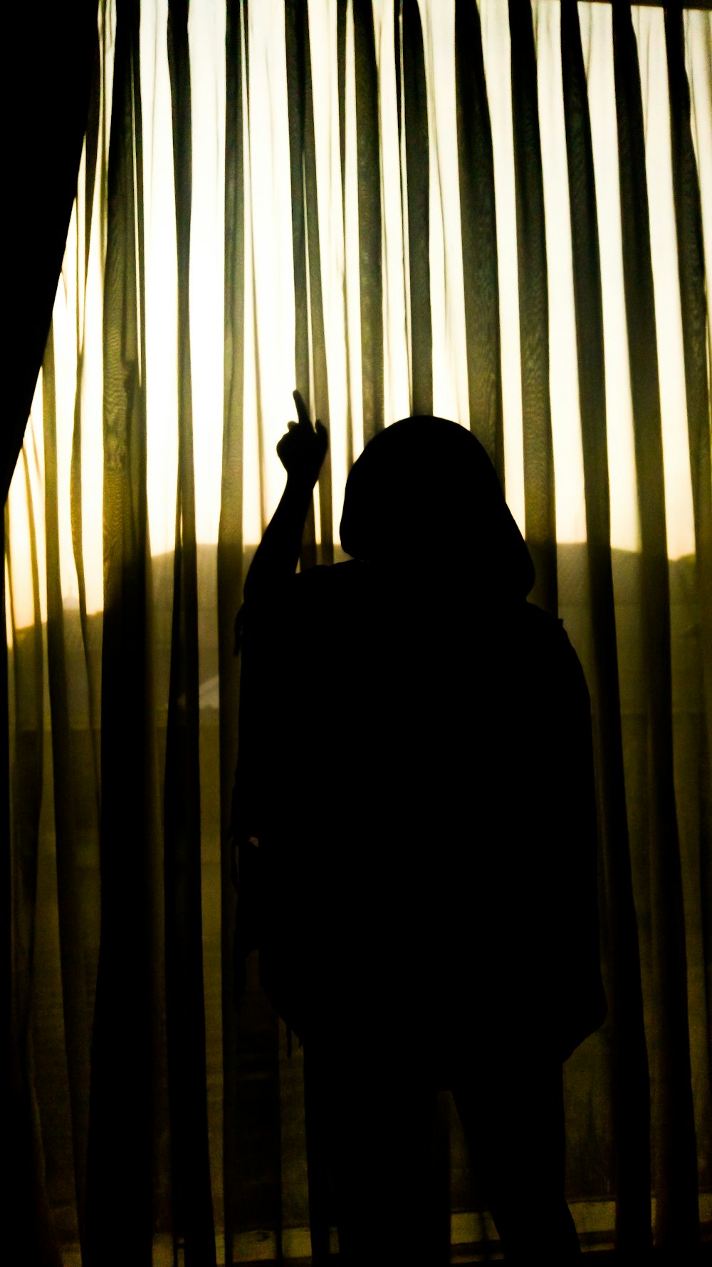 silhouette of person standing near window curtain