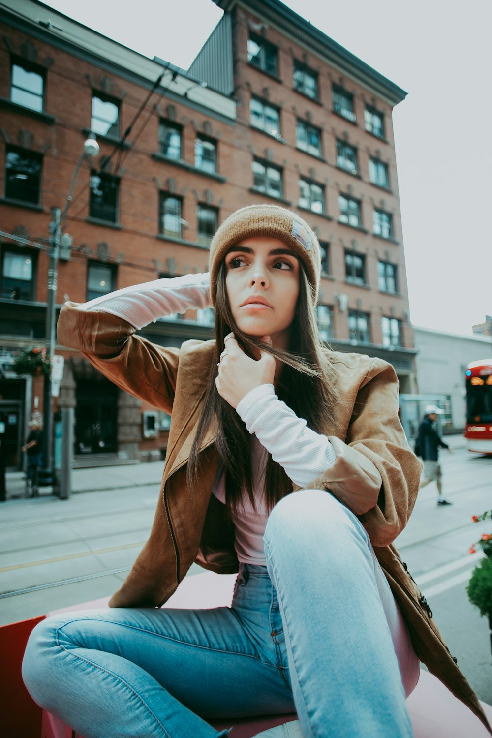 woman in brown coat and blue denim jeans sitting on sidewalk during daytime