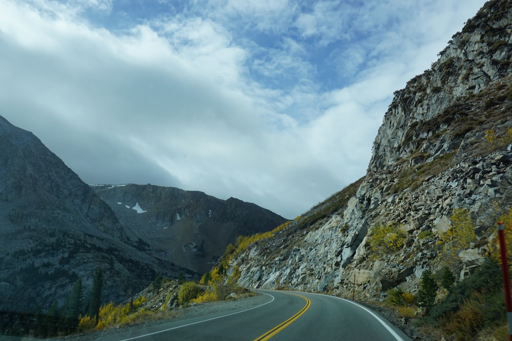 strada di cemento grigio vicino alla montagna sotto nuvole bianche durante il giorno