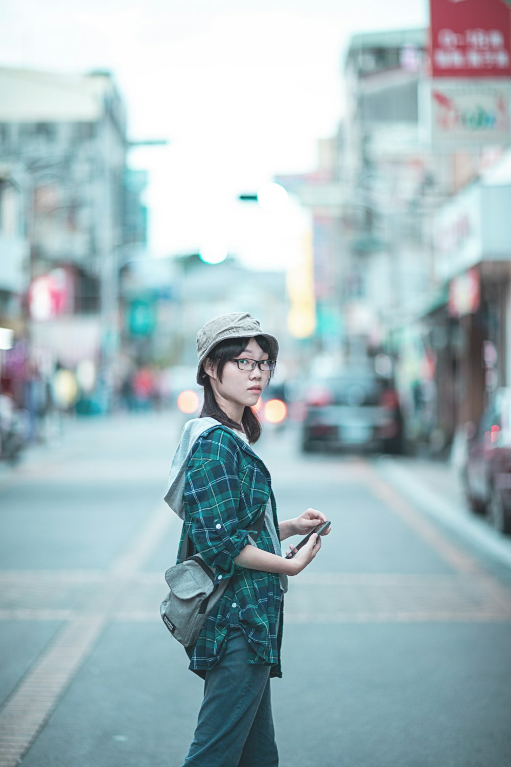 woman in black and white plaid dress shirt and black hat standing on sidewalk during daytime