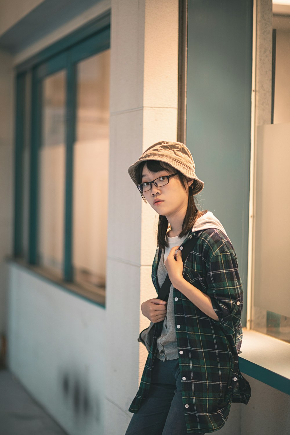 woman in black and white plaid dress shirt wearing brown hat standing beside white wall during