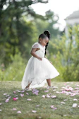 Toddler girl wearing a dusty pink dress with delicate lace, playing in a sunlit garden.