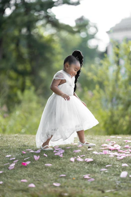 Toddler girl wearing a dusty pink dress with delicate lace, playing in a sunlit garden.