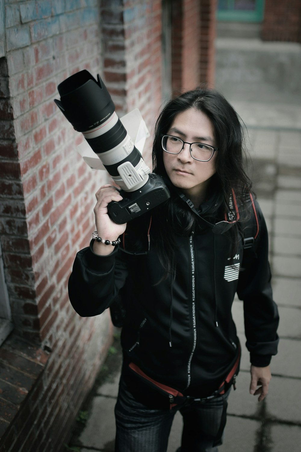 Femme en veste noire tenant un appareil photo reflex numérique noir et blanc