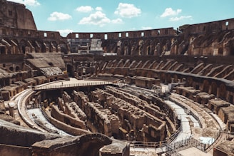 A view of the ancient Roman Colosseum showcasing its intricate architecture. The image captures the elliptical structure with its multiple levels of arches and the central arena. The exposed underground passages, which were once covered, are clearly visible. The stone and brickwork exude a sense of historical grandeur.