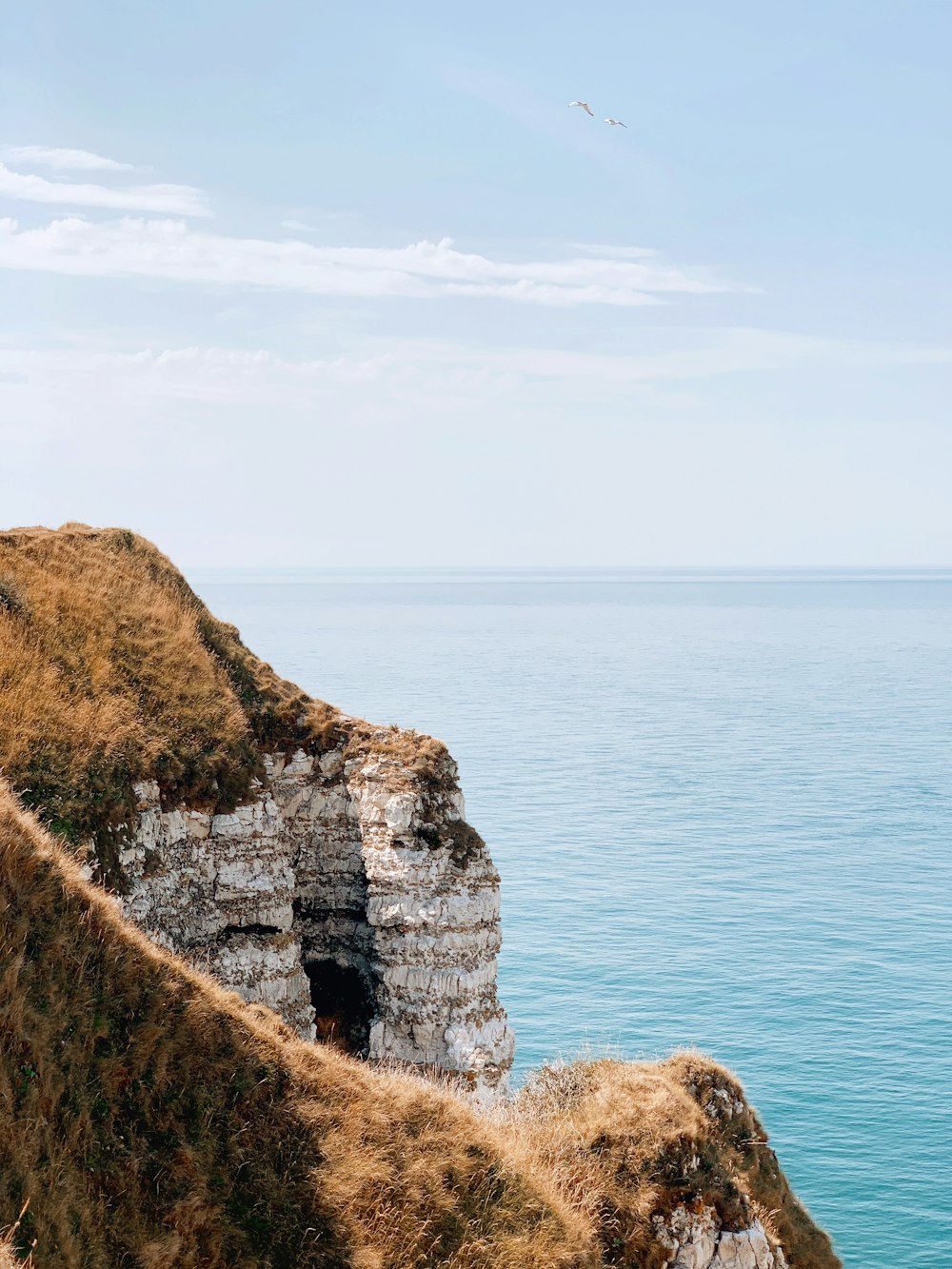 brown and green rock formation beside blue sea under white clouds during daytime