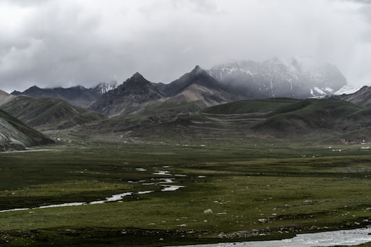 green grass field near mountain under white clouds during daytime in Tibet China