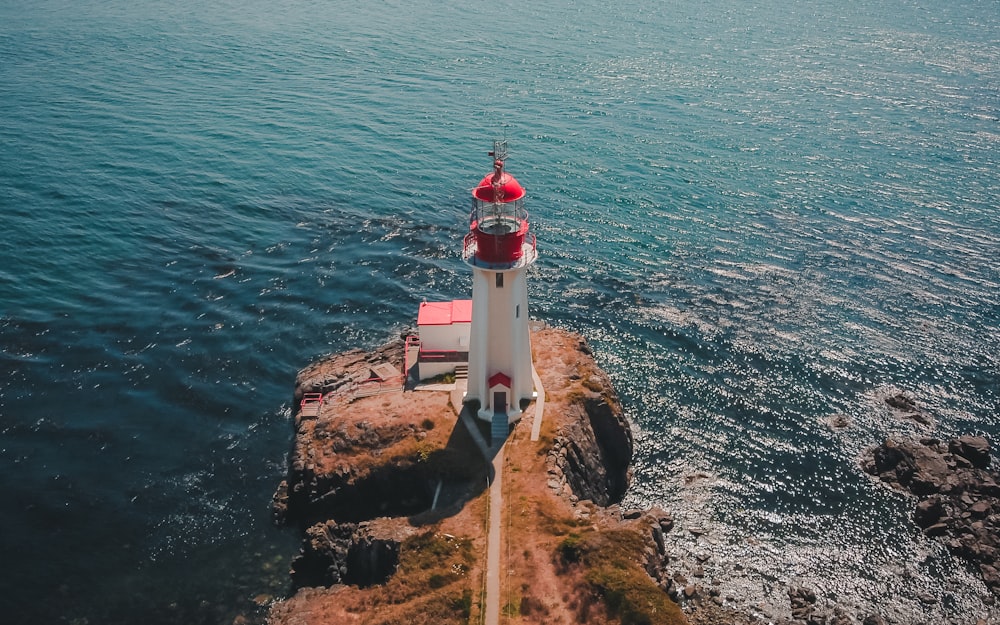 Phare blanc et rouge près d’un plan d’eau pendant la journée